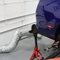 Dyno exhaust hose and nozzle attached to the tailpipe of a vehicle.