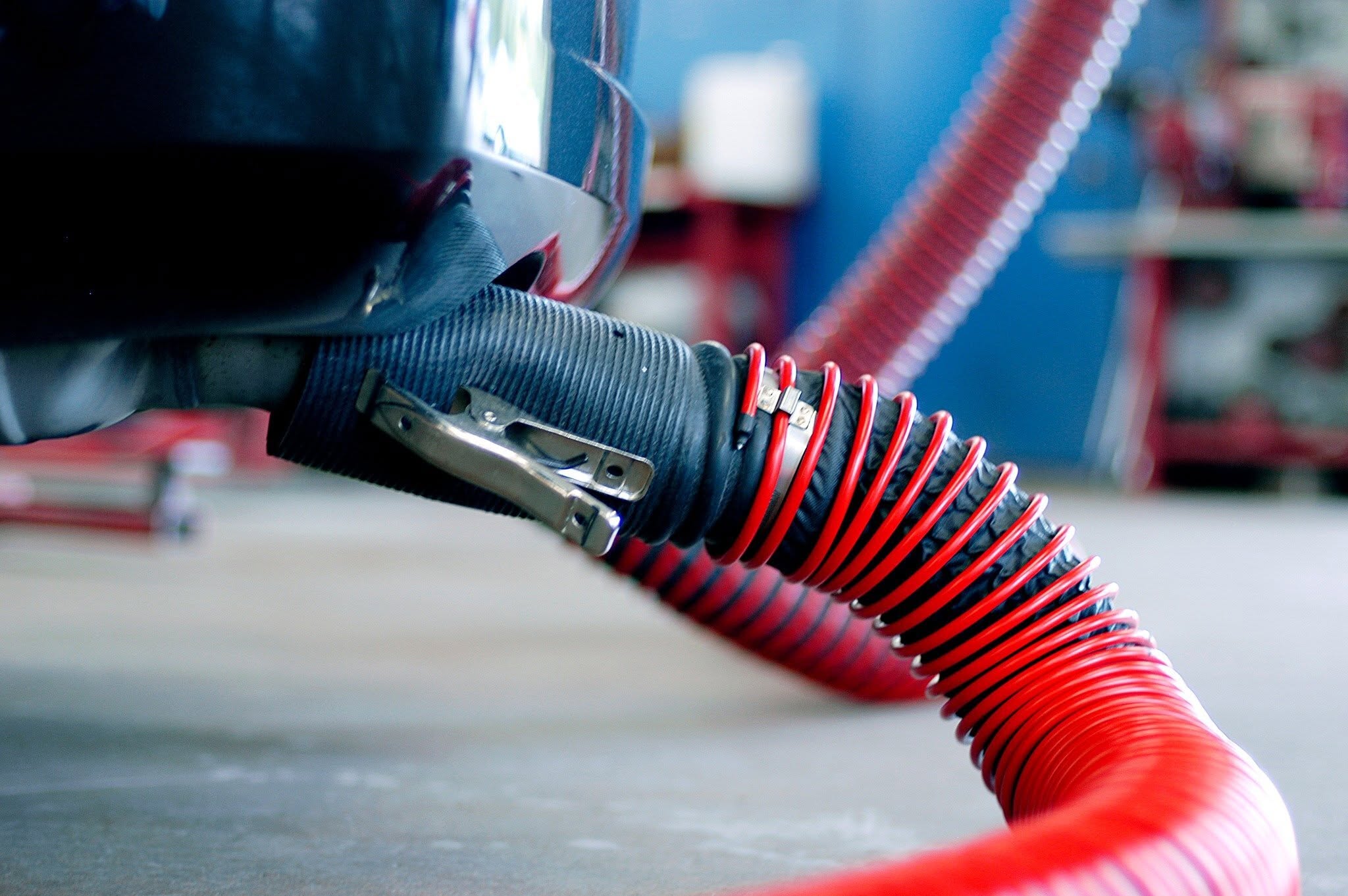 Tailpipe adapter clamped to a vehicle exhaust, connected to a red high-temperature exhaust hose at Hollywood Motor Co.