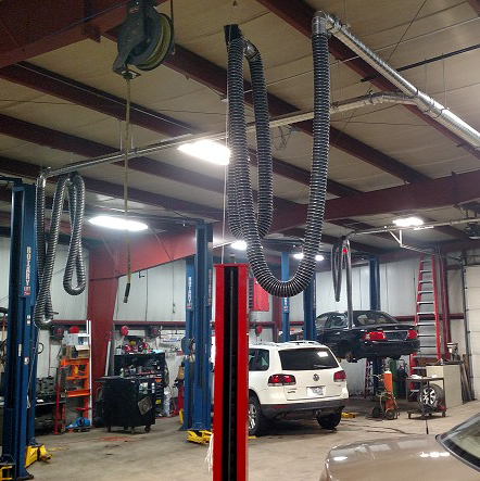 Overhead exhaust removal systems shown in a vehicle repair and maintenance shop.